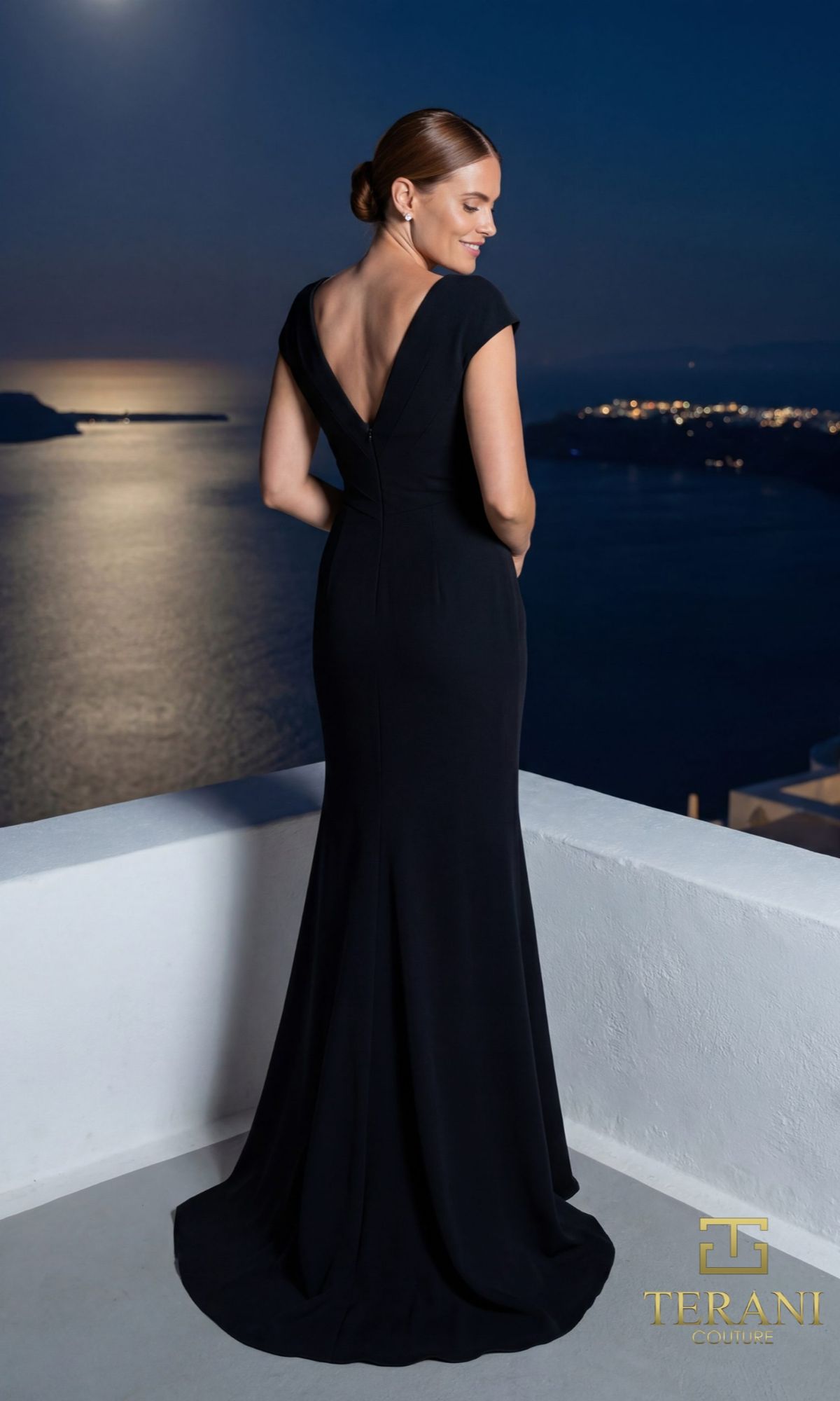 A woman in the Terani 261E6721 long formal dress stands on a balcony at night, gazing at the moonlit sea and illuminated coastline—a scene worthy of this elegant black crepe sheath.